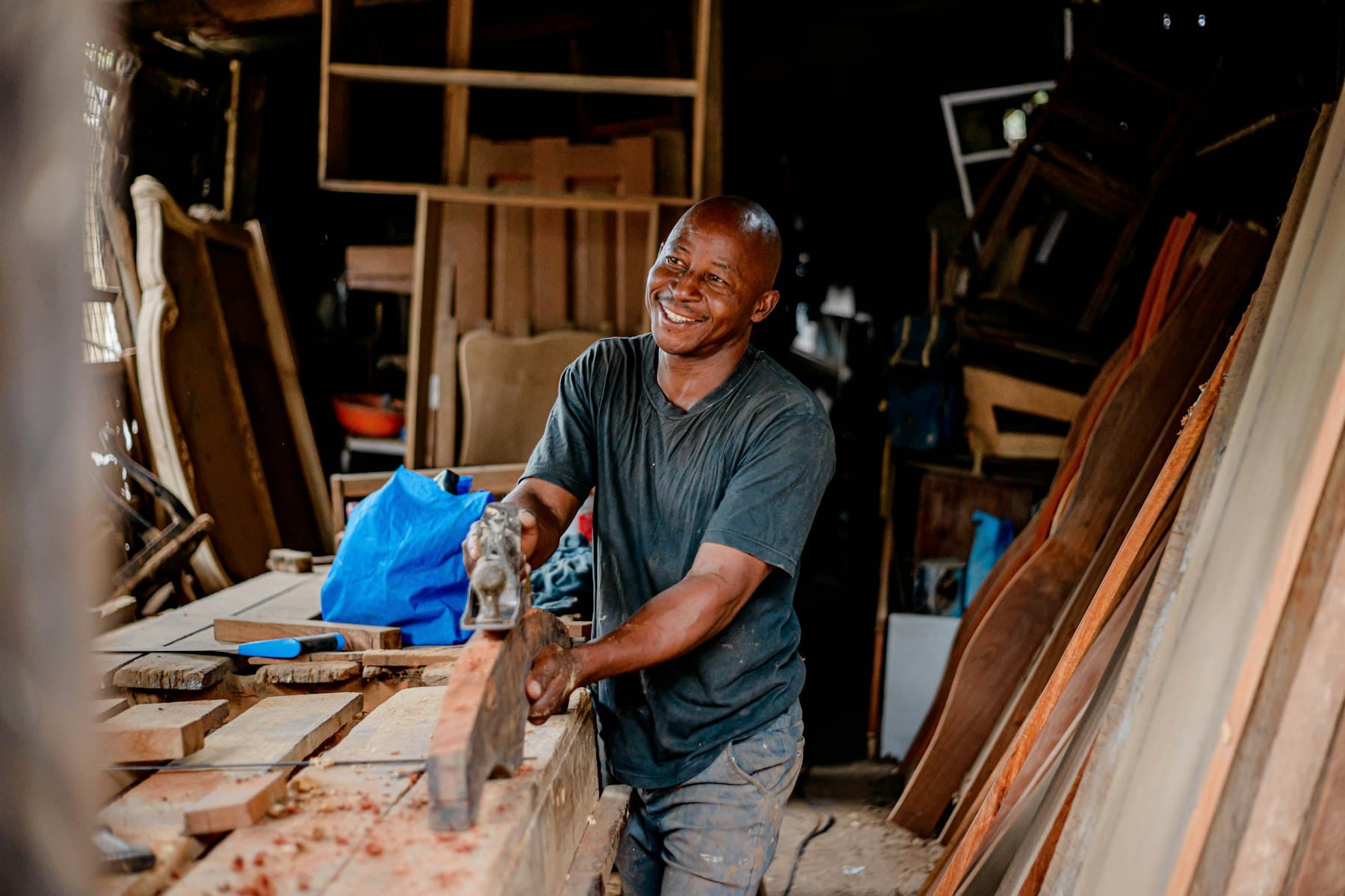 A carpenter smiling as he works on a piece of wood.